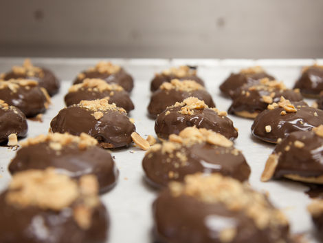 Chocolate covered cookies with peanut crumble on a baking sheet at Cookie Time Bakery