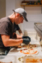 Marco adding toppings to pizzas