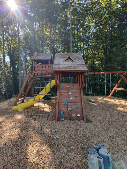 Wooden playset featuring yellow slide, climbing wall, swings, and wood chips