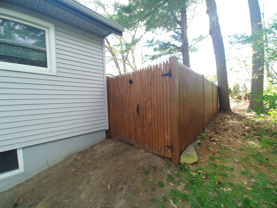 Dark brown wooden fence installed next to a light house and trees