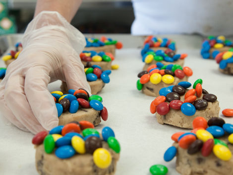 A hand arranging colorful candies on cookie dough. Cookie Time Bakery.