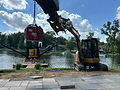 Excavator lifts machine near lake