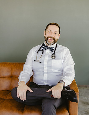 Smiling Dr. Nemero with stethoscope and bowtie on leather sofa.