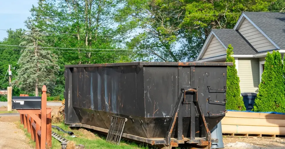 A large roll-off dumpster sits on a platform on a home's lawn with patches of dirt and trimmed shrubbery.