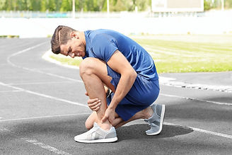 Athletic man outdoors grabbing his foot or ankle in pain.