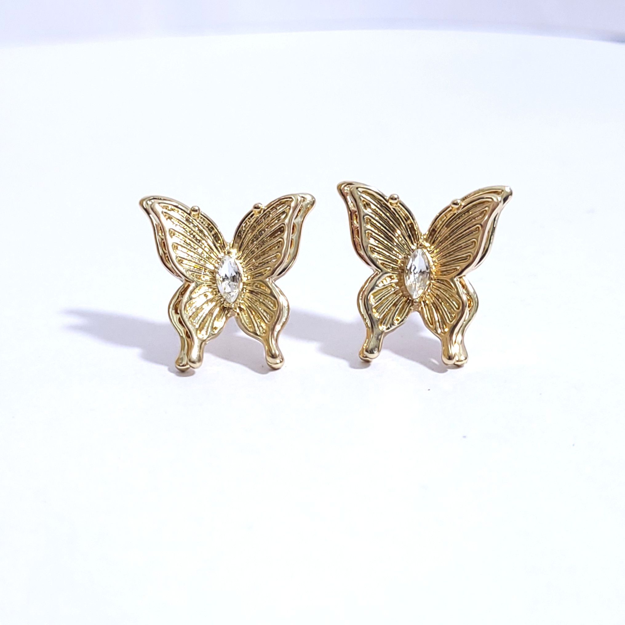 Pair of gold butterfly-shaped stud earrings with a clear crystal center on a white background.