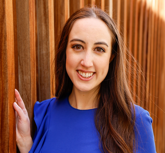 An image of Maya, founder of Organized and Inspired. She is wearing a blue dress against a wooden background.