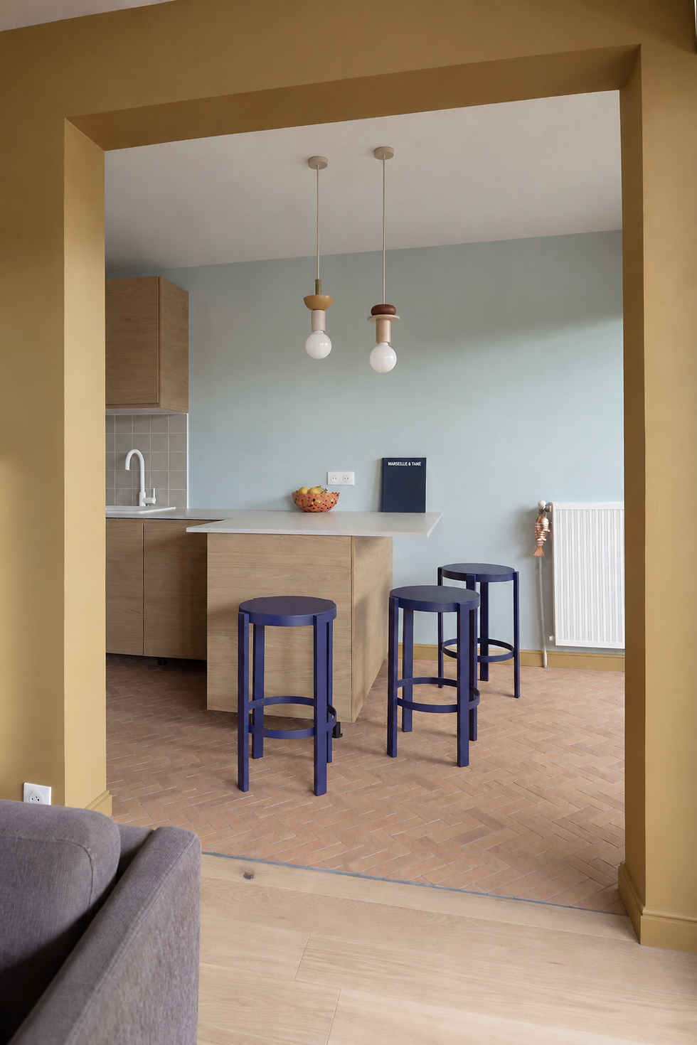 Cuisine rénovée en bois clair avec mur bleu, plan snack et tabourets bleu profond – projet Maison Idéale à Marseille