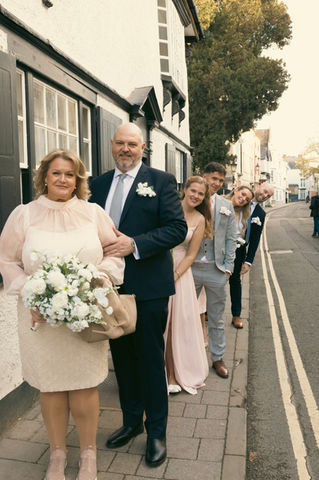 Group of wedding guests lined up along a pavement on an Oxford street in a playful, quirky pose, wearing formal wedding attire against historic city buildings