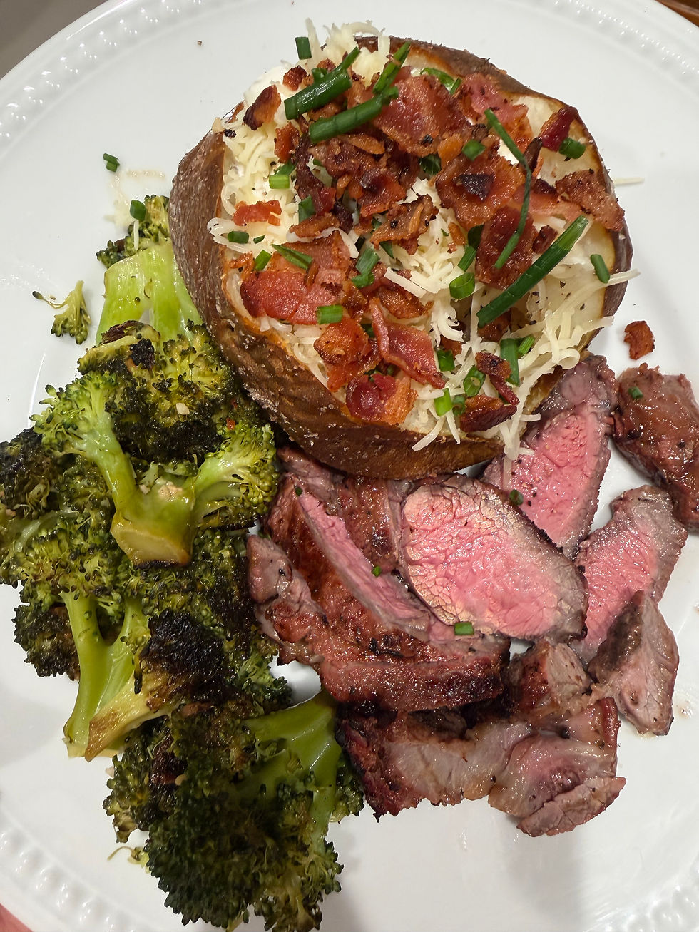 a beautifully plated steak dinner with a loaded baked potato and broccoli