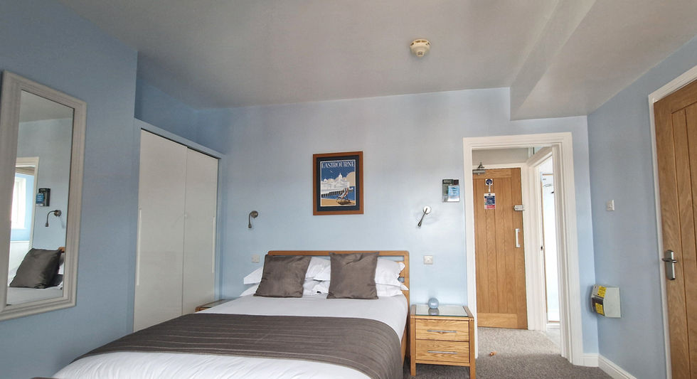 Beachside Eastbourne Apartment 4 studio loft with sloped white ceilings, a quilted bed runner, and a brown sofa.