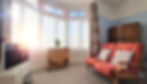 Bright and cozy living room in Eastbourne holiday rental with comfortable red sofas, a wooden coffee table, and a flat-screen TV, illuminated by natural light from large windows with stained glass details.