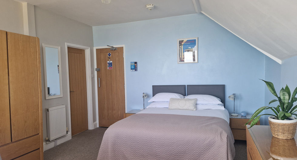 Spacious bedroom in Beachside Eastbourne Apartment 5 featuring a king size bed, neutral tones, wooden furniture, and light blue walls under a sloped ceiling.