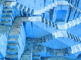 Intricate blue stone stepwell with geometric patterns, viewed from above. The setting creates an abstract and serene mood.