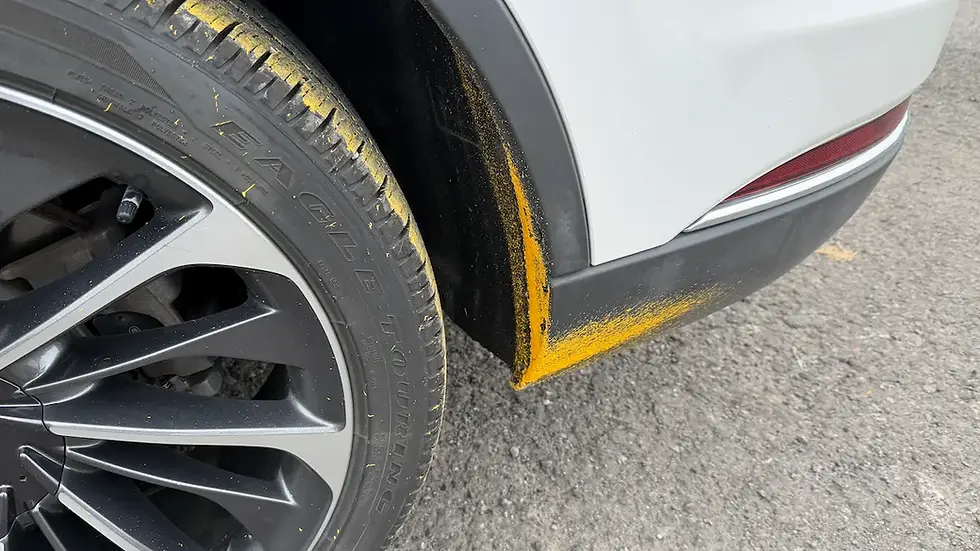 Yellow road line paint splattered across a vehicle’s tire, wheel well, plastic trim and painted rear bumper.