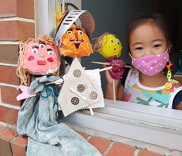 A young girl wearing a mask, holding hand-made puppets.