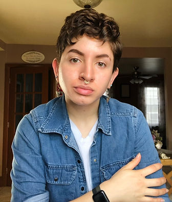 A person with short brown hair wearing a denim shirt in front of a brown background