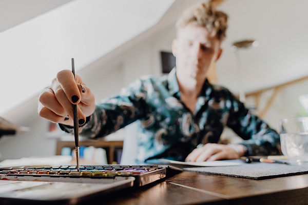 Marius tunkt einen Pinsel in Aquarellfarbe. Was er wohl damit macht?
