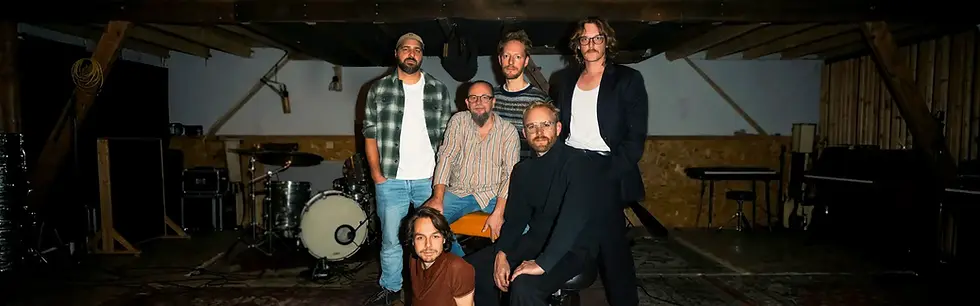 Bandleden poseren bij muziekinstrumenten in een oefenruimte.