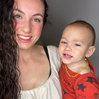 Smiling woman with long, thick, dark curly hair taking a close-up selfie with her happy young toddler. The toddler wears a red star-patterned shirt and a yellow beaded necklace.
