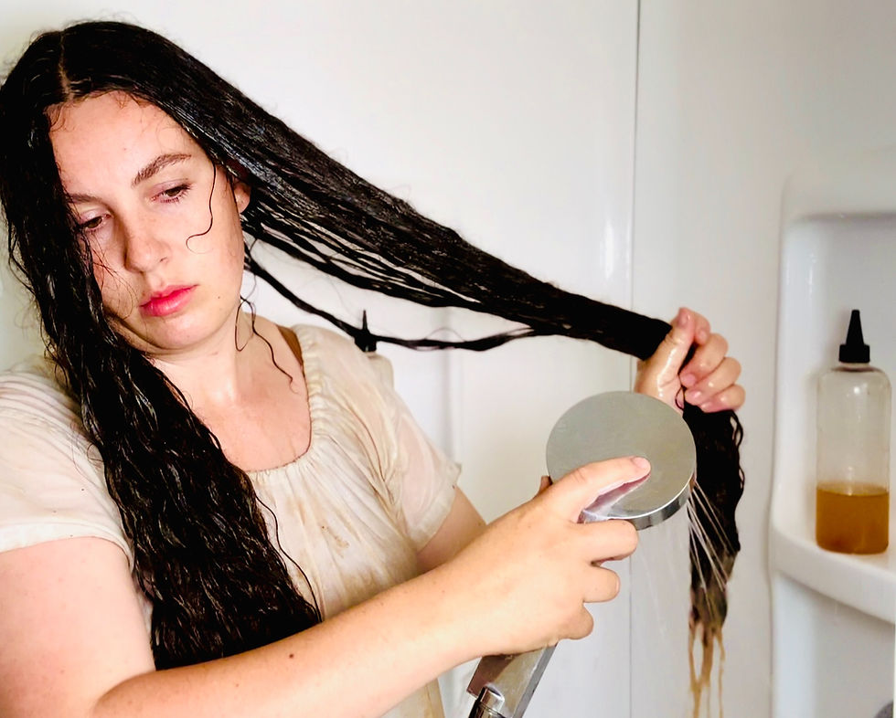 Woman with long hair rinsing wet strands under shower in bathroom, demonstrating infrequent hair washing method for length retention and preserving natural oils, modern take on Edwardian long hair care secrets