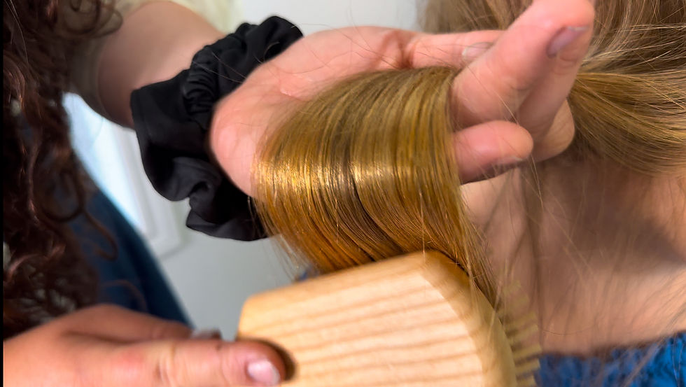A closeup of a woman brushing another woman's hair gently with a wooden bristle brush.