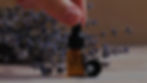 Hand holding a dropper with an amber bottle, cap off, surrounded by lavender flowers on a wooden surface. Warm, calming ambiance.
