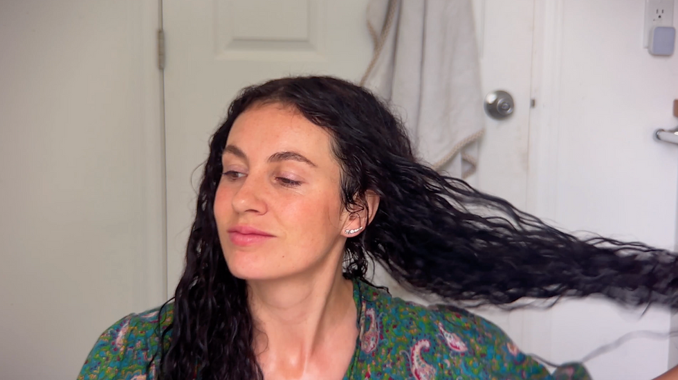 Woman with long, wet, dark wavy hair looking softly to the side after washing, her strands appearing clean, shiny, and conditioned — the final soft and healthy results from using the DIY African black soap shampoo recipe.