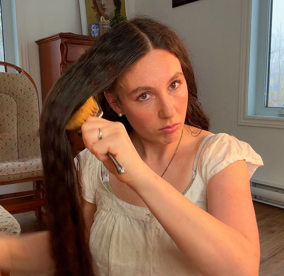 Woman with floor-length dark hair brushing thick section from roots to ends using 100% boar bristle brush in cozy room, daily Edwardian-inspired hair care routine for distributing natural oils, scalp massage, and length retention following Aline Vallandri's 1912 advice