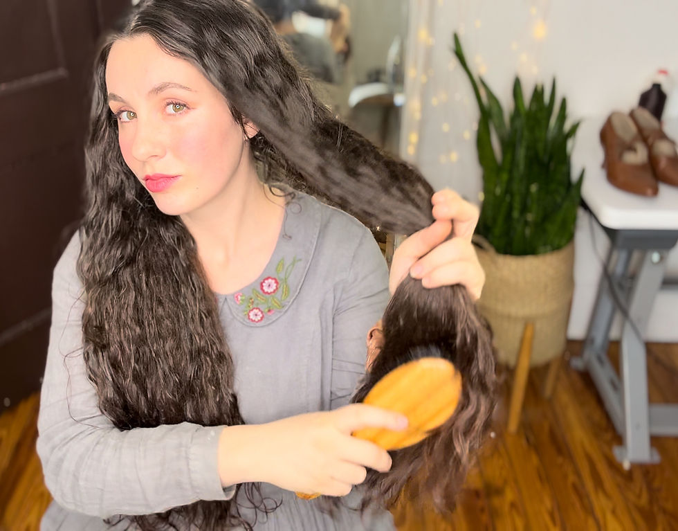 Woman with long dark wavy hair holding a section of her hair and brushing it with a wooden boar bristle brush.