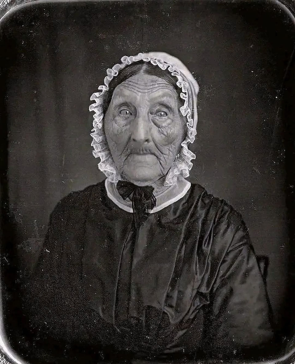 Victorian-era elderly woman with naturally dark hair in a formal 19th-century daguerreotype portrait wearing a white ruffled bonnet