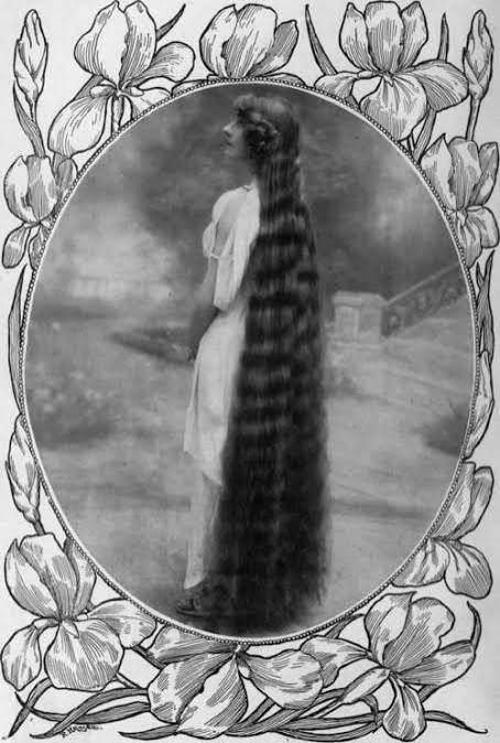 Aline Vallandri Edwardian opera singer with legendary floor-length hair, vintage Art Nouveau portrait in oval frame surrounded by magnolias and irises, long flowing dark locks cascading to ground, ethereal gown and romantic Belle Époque aesthetic