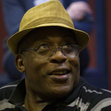 Smiling man wearing glasses and hat, wearing a striped shirt indoors.
