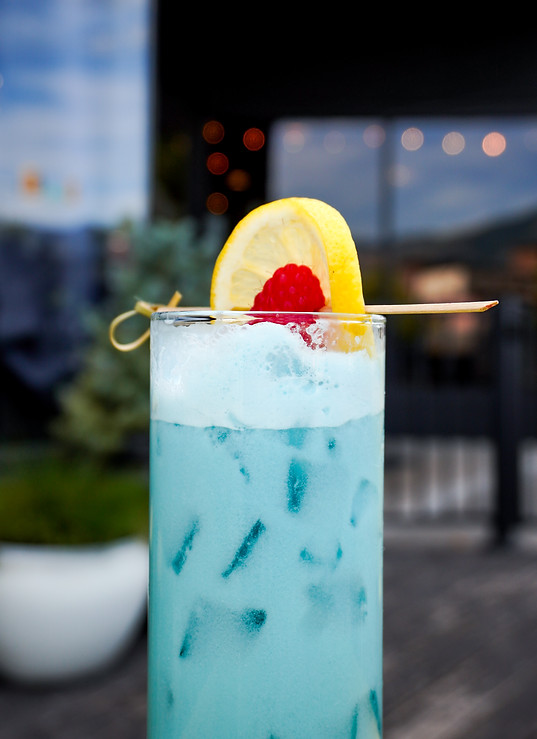 blue cocktail with lemon and raspberry garnish