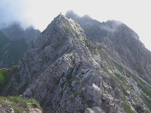 Ein felsiger Berggipfel auf dem zwei Bergsteiger stehen.