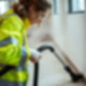 a woman wearing high visibility clothes cleaning dust and debris with a vacuum.jpg