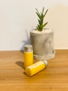 líquido amarillo-naranja en un vaso, cerca de una planta, debajo de una planta: ilustrando la toma de naranja y jengibre
