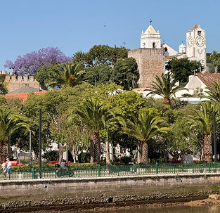Tavira old town with castle walls and church clock tower above the riverside palms