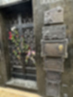 Ornate black mausoleum door adorned with red and white flowers on a marble wall featuring engraved plaques with text, creating a solemn mood.