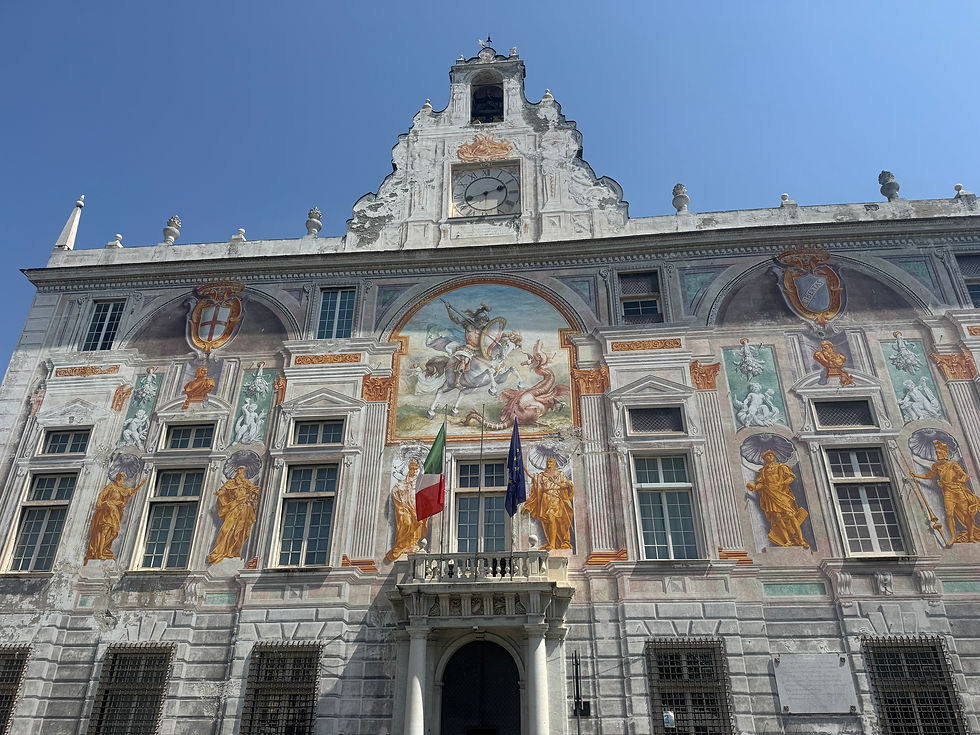 Ornate historic building facade with clock, murals and statues; Italian and EU flags hang below a bright blue sky.