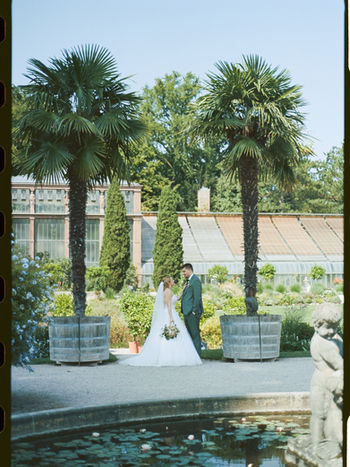 Brautpaar am Pool zwischen Palmen und mediterraner Architektur, aufgenommen mit analoger Filmfotografie