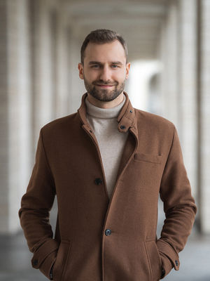 Ein Mann steht in einem braunen Mantel im Hintergrund der Stadt. Sehr klares und einfaches Hintergrund.
