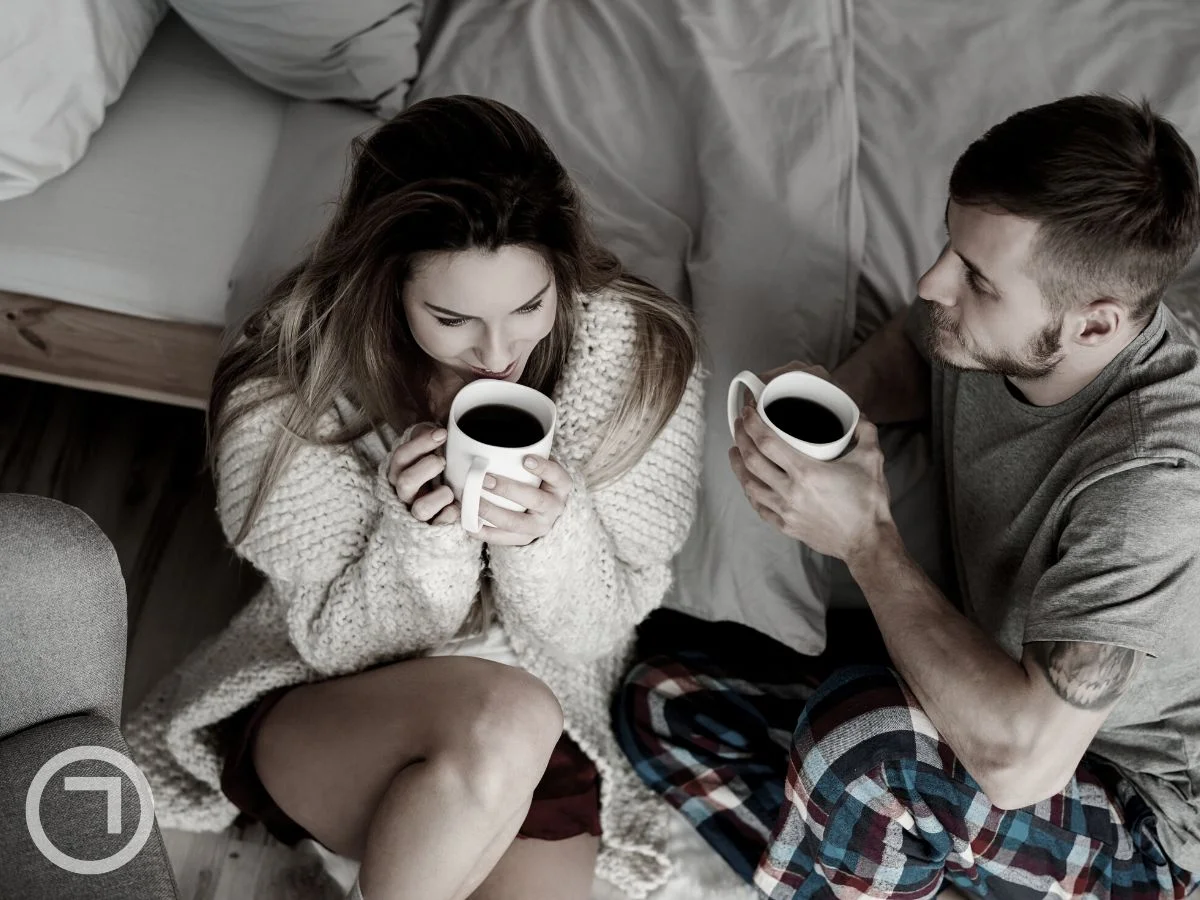 A couple laying on bed and having tea/coffee