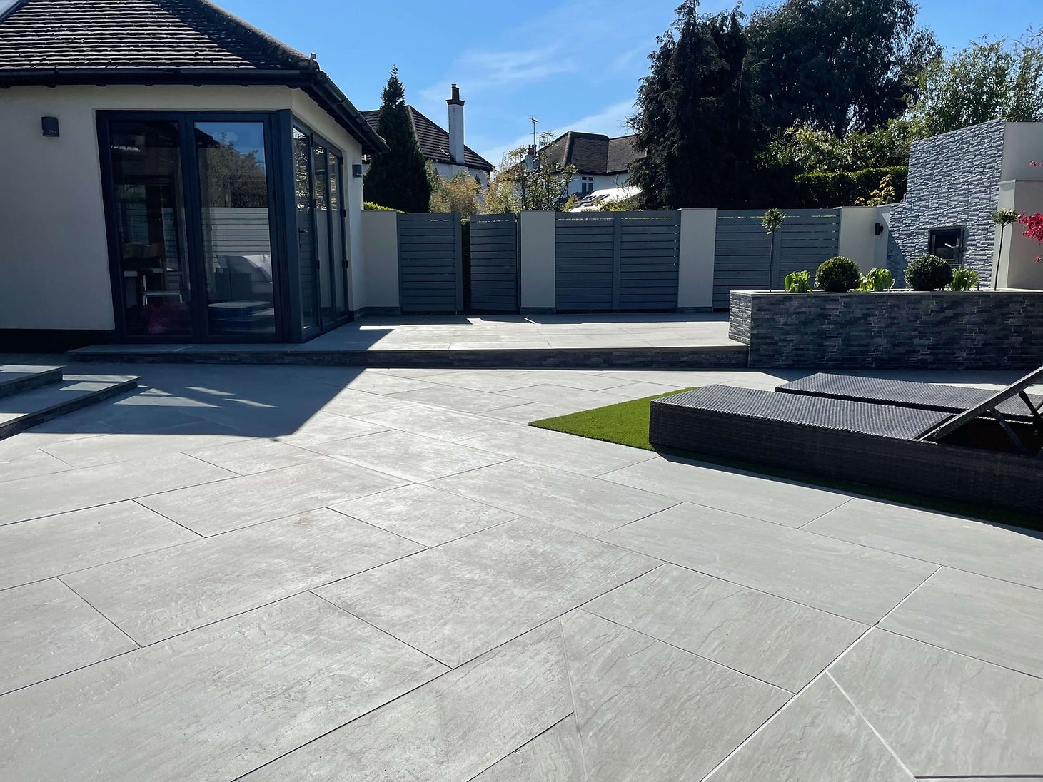 Hard-landscaped garden with porcelain tiles and grassed sun-lounging near a garden room