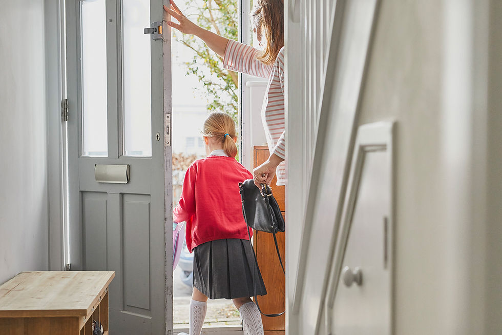 A mother holding the front door open for her young daughter wearing her school uniform
