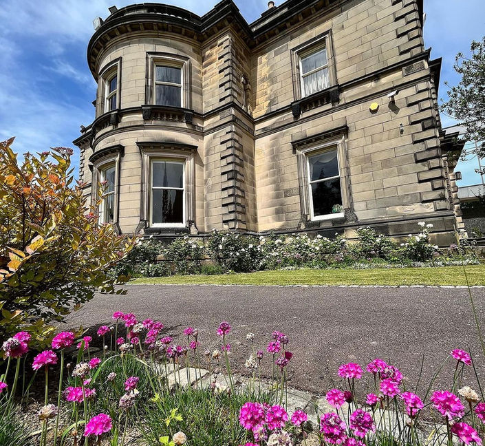 Low-angled photo of Tapton Hall with pink flowers in the foreground