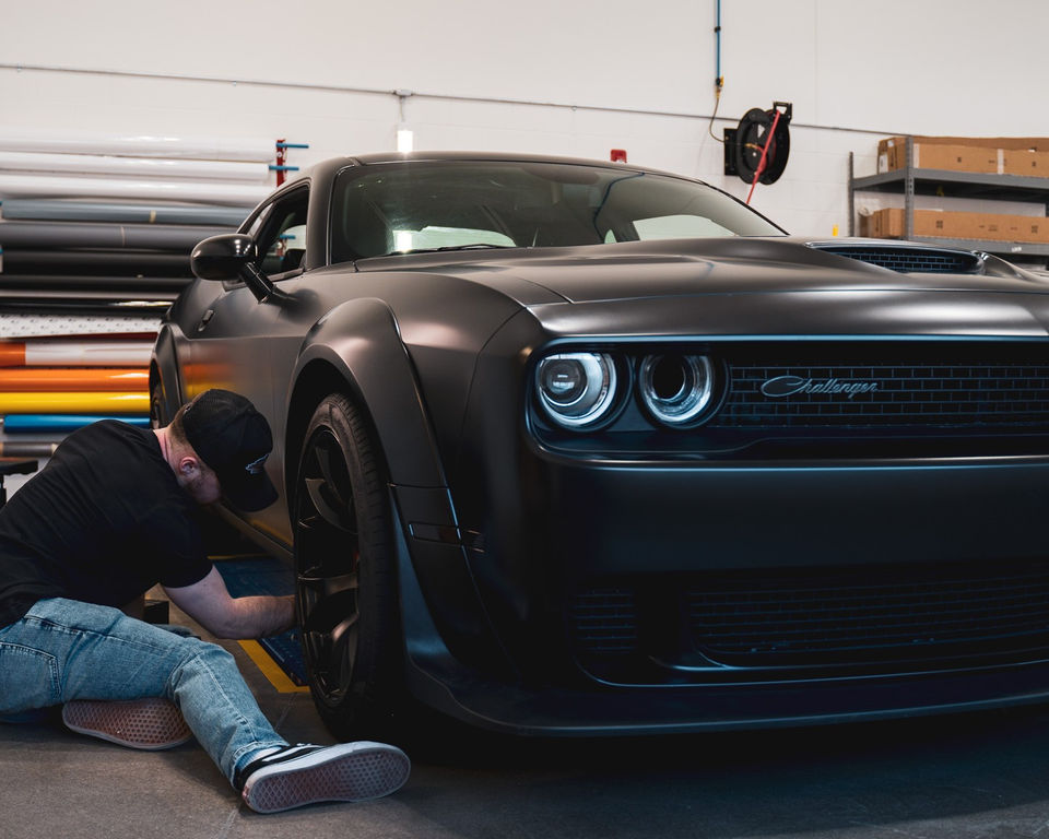 Luke Potter from Wrap Kingz applying a custom matte black wrap on a Dodge Challenger.