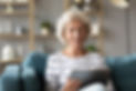 Calm mature woman using computer tablet, looking at screen, sitting on couch at home