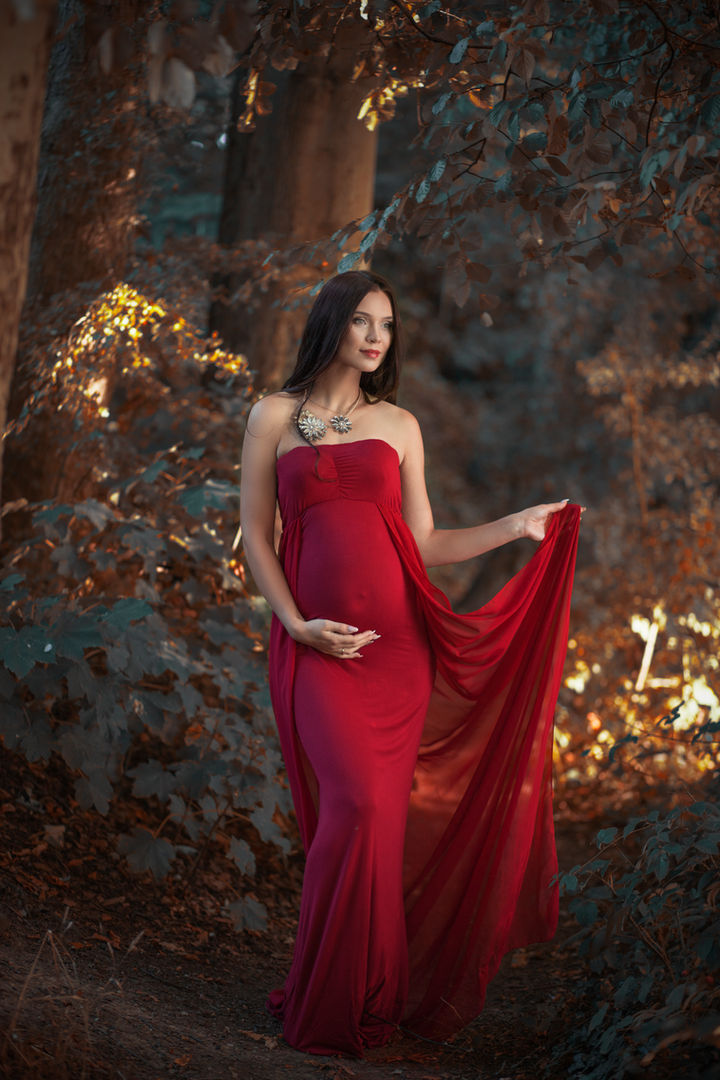 Elegant outdoor maternity photo of a glowing pregnant woman in a flowing gown, cradling her baby bump at sunset. Captured in soft natural light, this serene portrait highlights the beauty of motherhood and the joy of expecting. Ideal for maternity photography inspiration, pregnancy photoshoot ideas, and timeless keepsake images