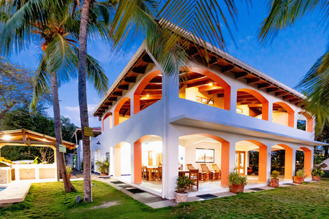 Modern two-story villa surrounded by palm trees, featuring arched windows and a spacious outdoor dining area.